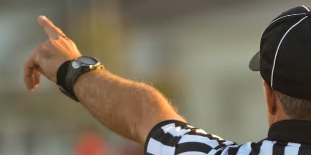 Árbitro con reloj en la muñeca señalando una jugada